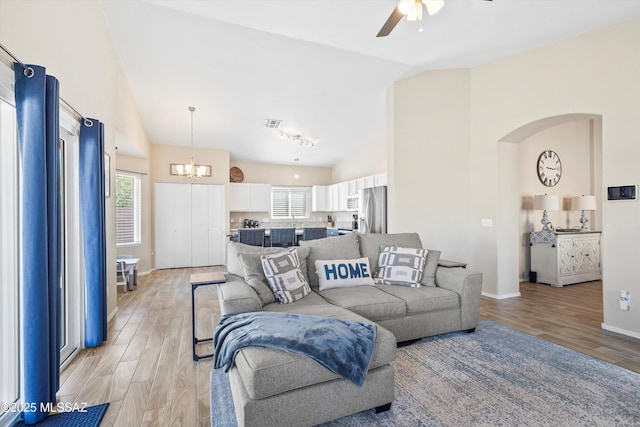 living room with arched walkways, baseboards, light wood-style flooring, high vaulted ceiling, and ceiling fan with notable chandelier