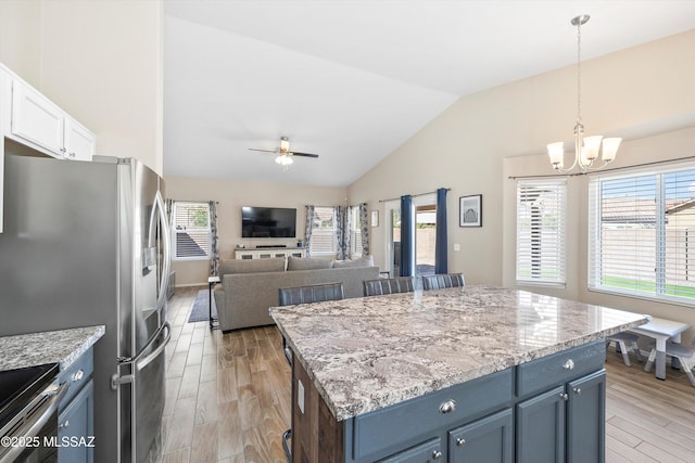 kitchen featuring light wood finished floors, a center island, vaulted ceiling, ceiling fan with notable chandelier, and light stone counters
