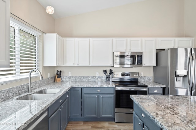 kitchen featuring lofted ceiling, stainless steel appliances, blue cabinets, a sink, and white cabinetry