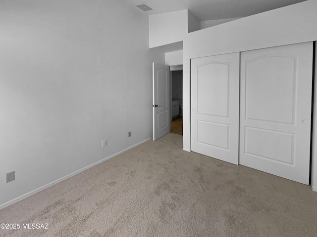 unfurnished bedroom featuring a closet, visible vents, carpet floors, lofted ceiling, and baseboards