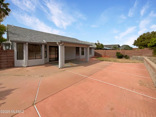 rear view of house with a patio, stucco siding, a fenced backyard, and a shingled roof