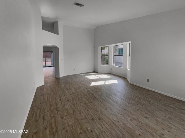 empty room with visible vents, arched walkways, plenty of natural light, and dark wood finished floors