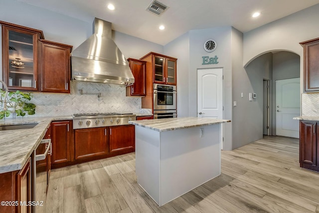 kitchen with visible vents, wall chimney range hood, arched walkways, a sink, and appliances with stainless steel finishes