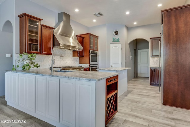 kitchen featuring visible vents, arched walkways, tasteful backsplash, ventilation hood, and a peninsula