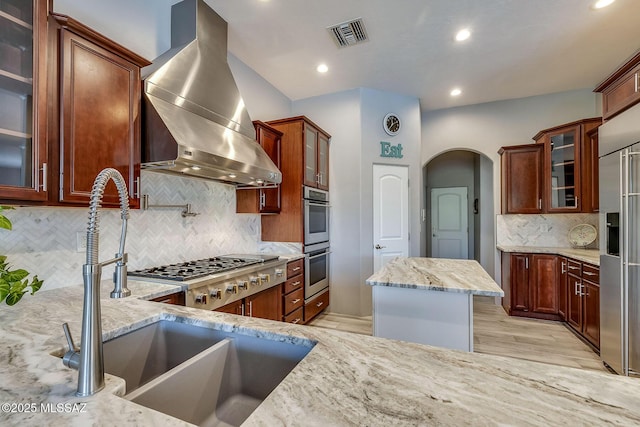 kitchen with light stone counters, backsplash, wall chimney exhaust hood, and visible vents