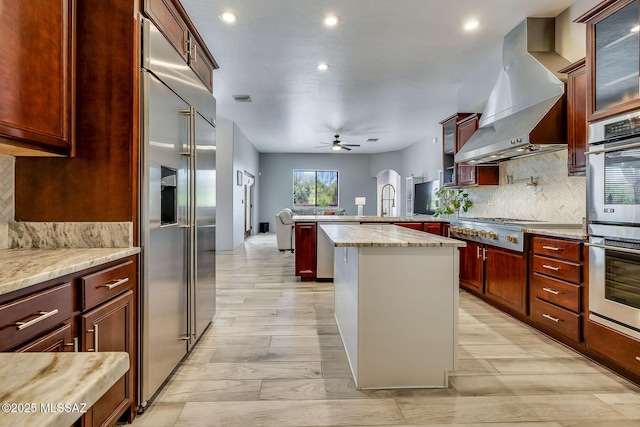 kitchen with ceiling fan, appliances with stainless steel finishes, tasteful backsplash, ventilation hood, and a peninsula