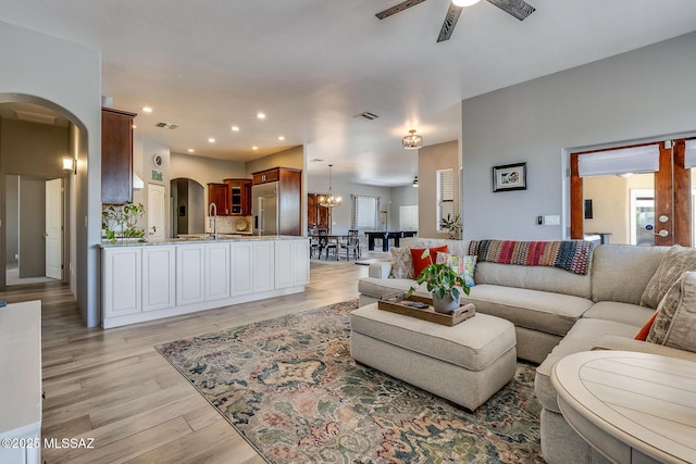 living room featuring plenty of natural light, a ceiling fan, visible vents, arched walkways, and light wood-type flooring