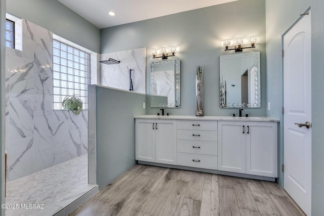 bathroom featuring double vanity, a sink, a marble finish shower, and wood finished floors