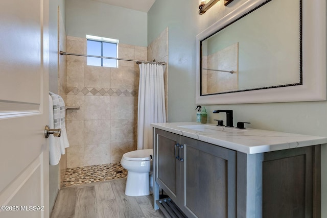 full bathroom with toilet, a tile shower, wood finished floors, and vanity