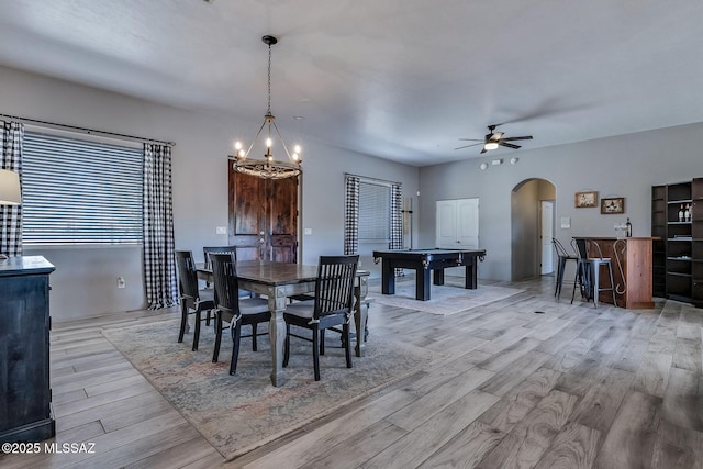 dining space featuring arched walkways, ceiling fan with notable chandelier, light wood finished floors, and pool table