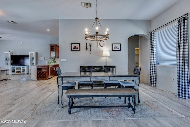 dining room featuring arched walkways, light wood-type flooring, a chandelier, and visible vents