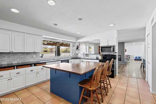 1932 W Harran Cir, Tucson, AZ 85704 - kitchen with stainless steel microwave, range with electric stovetop, backsplash, a breakfast bar, and white cabinetry