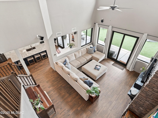 living room with visible vents, wood finished floors, a towering ceiling, and a healthy amount of sunlight