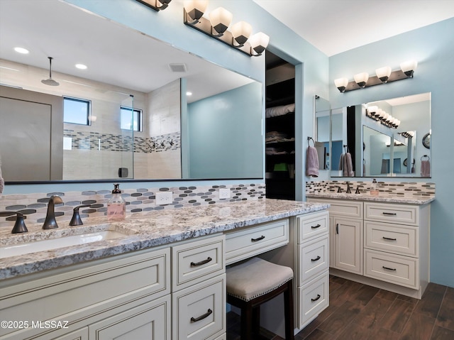 bathroom featuring a shower stall, vanity, visible vents, wood finished floors, and backsplash