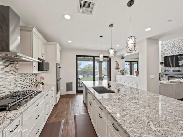 kitchen with visible vents, wall chimney exhaust hood, a sink, decorative backsplash, and stainless steel gas cooktop