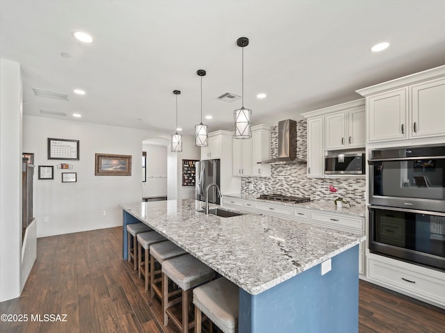 kitchen with a kitchen island with sink, wall chimney exhaust hood, a kitchen bar, appliances with stainless steel finishes, and a sink