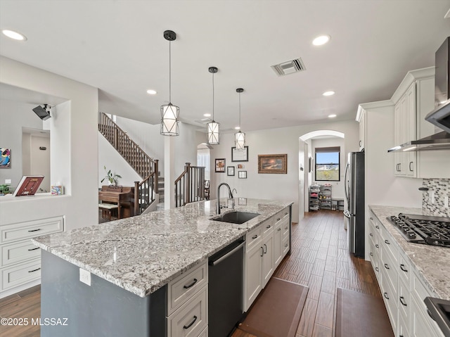 kitchen featuring visible vents, a center island with sink, stainless steel appliances, arched walkways, and a sink