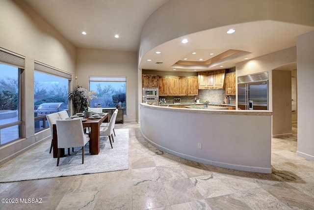 kitchen featuring brown cabinetry, built in appliances, backsplash, baseboards, and recessed lighting