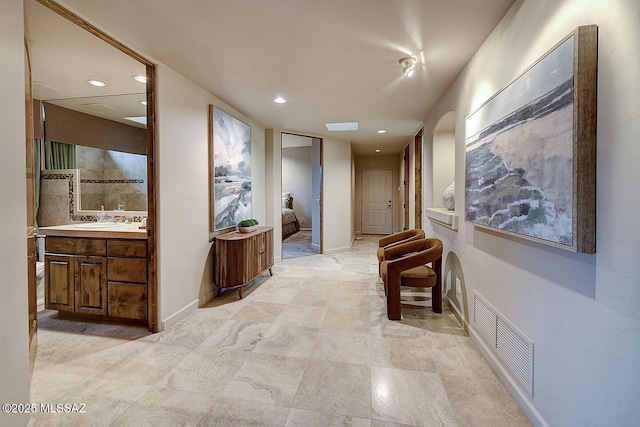 hall featuring baseboards, visible vents, recessed lighting, and a sink