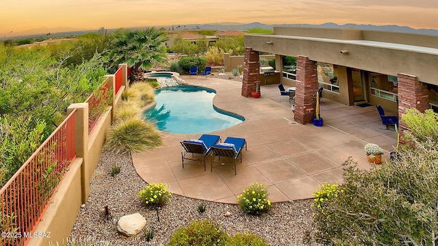 pool at dusk featuring a patio area, a fenced in pool, and an in ground hot tub