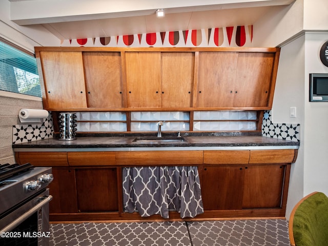 kitchen with stainless steel range with gas stovetop, a sink, backsplash, and dark countertops