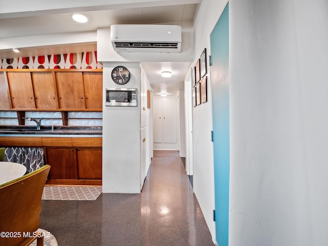 kitchen featuring dark speckled floor, a wall mounted air conditioner, stainless steel microwave, brown cabinets, and a sink