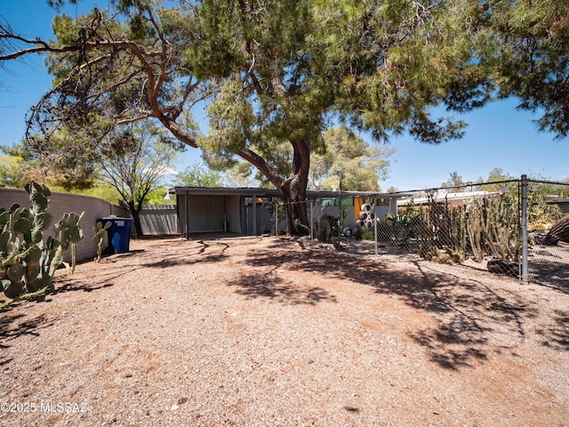 view of yard featuring dirt driveway, a detached carport, and fence