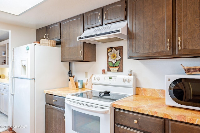 kitchen featuring dark brown cabinetry, under cabinet range hood, and white appliances