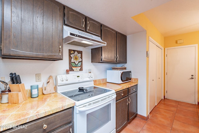 kitchen featuring dark brown cabinets, light tile patterned floors, under cabinet range hood, and white appliances