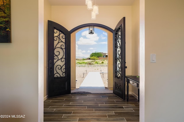 foyer featuring arched walkways, wood finish floors, a chandelier, and baseboards