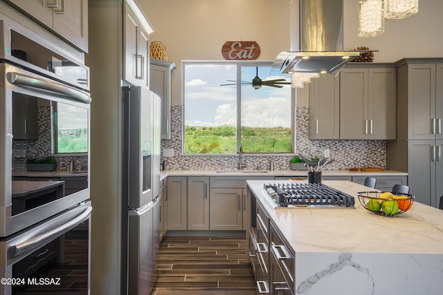 kitchen featuring island exhaust hood, tasteful backsplash, a sink, gray cabinetry, and stainless steel appliances
