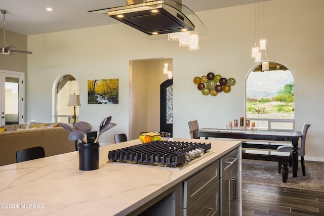 kitchen featuring light stone counters, stainless steel gas cooktop, arched walkways, open floor plan, and dark wood-style floors