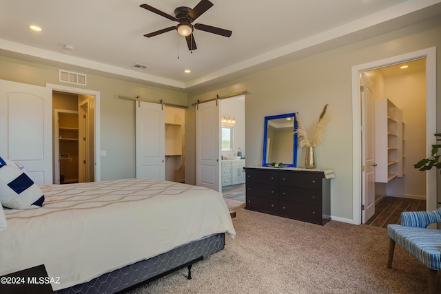 carpeted bedroom with a spacious closet, a barn door, ensuite bathroom, and visible vents
