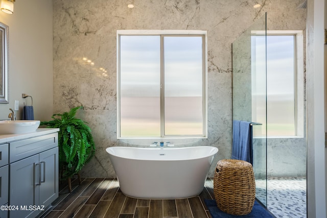 bathroom featuring tile walls, wood finish floors, walk in shower, vanity, and a soaking tub