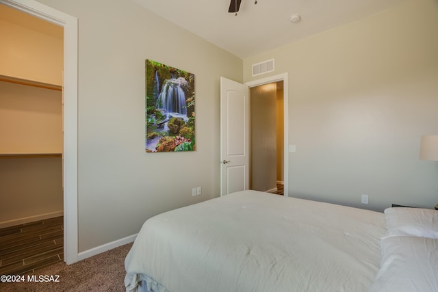 carpeted bedroom featuring visible vents, baseboards, a walk in closet, and ceiling fan