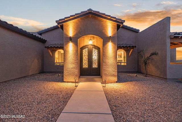 exterior entry at dusk featuring a tile roof and stucco siding