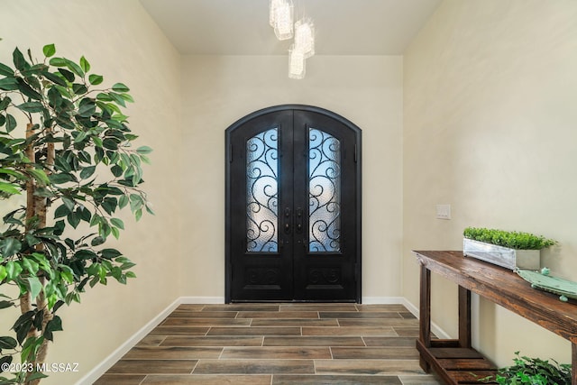foyer entrance with french doors, arched walkways, wood finish floors, baseboards, and an inviting chandelier