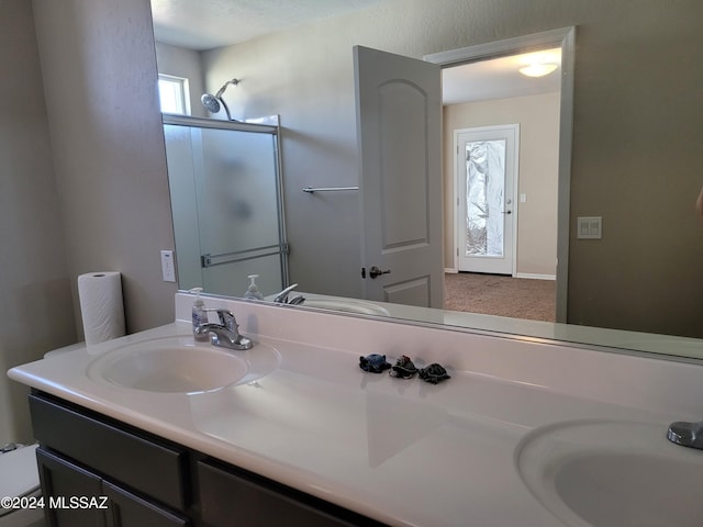 bathroom with a shower with shower door, double vanity, a sink, and a wealth of natural light