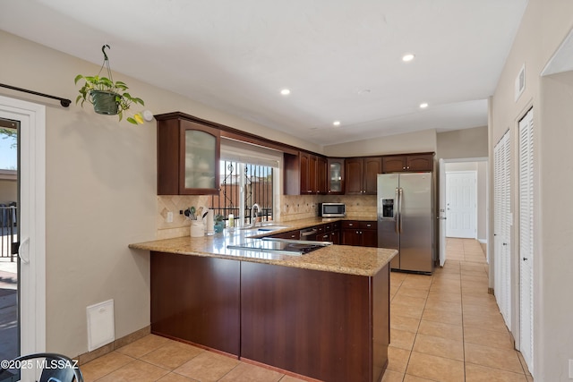 kitchen with stainless steel appliances, a sink, backsplash, a peninsula, and light stone countertops