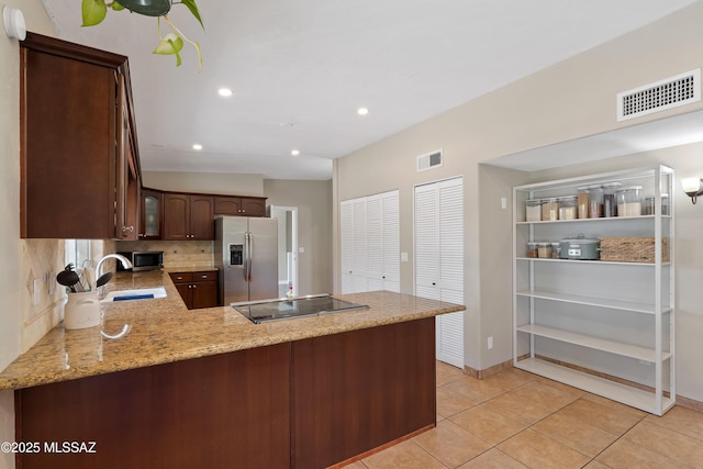 kitchen featuring appliances with stainless steel finishes, a sink, a peninsula, light tile patterned floors, and light stone counters