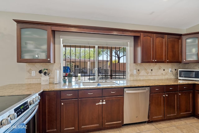 kitchen featuring stainless steel appliances, a sink, decorative backsplash, and light stone counters