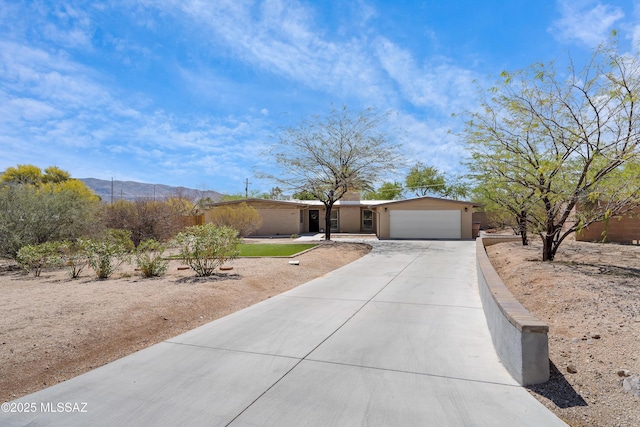single story home with a garage, a mountain view, concrete driveway, and stucco siding