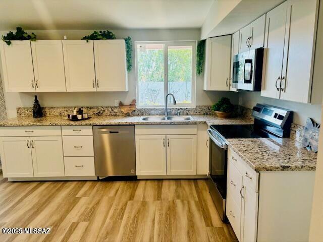 kitchen with light wood-type flooring, white cabinetry, appliances with stainless steel finishes, light stone counters, and a sink