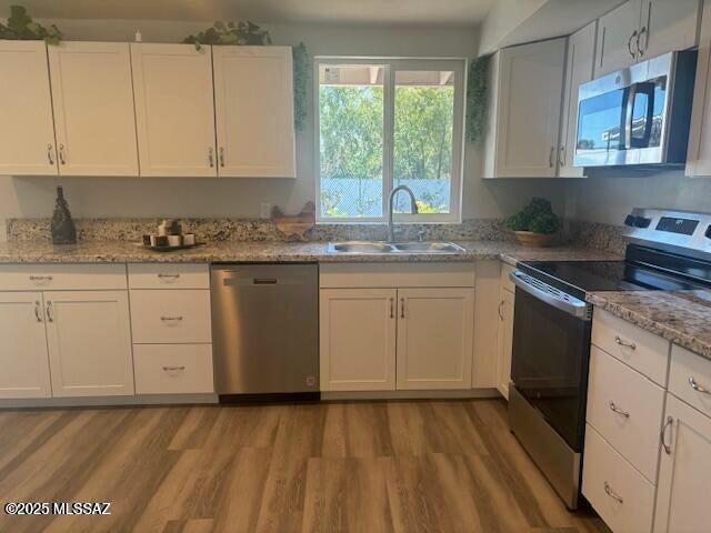 kitchen with stainless steel appliances, white cabinets, a sink, and wood finished floors