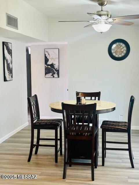 dining room with light wood finished floors, baseboards, a ceiling fan, and visible vents