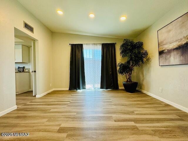 spare room with visible vents, baseboards, light wood-style flooring, and lofted ceiling
