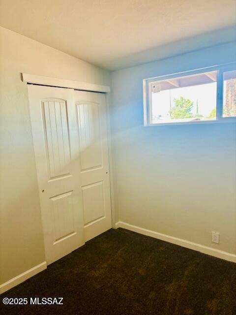 unfurnished bedroom featuring a closet, baseboards, and dark colored carpet