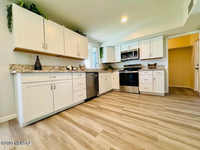 kitchen featuring light wood-type flooring, white cabinetry, appliances with stainless steel finishes, light stone counters, and baseboards
