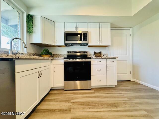 kitchen featuring baseboards, appliances with stainless steel finishes, light wood-style floors, white cabinetry, and light stone countertops