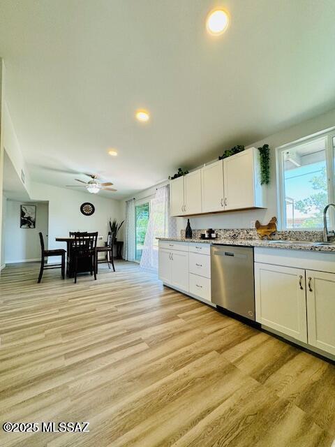 kitchen with stainless steel dishwasher, light wood-type flooring, a sink, and white cabinetry